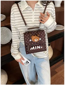 Sac brun à pois porté, avec ourson en peluche, inscription MINI et attaches métalliques visibles