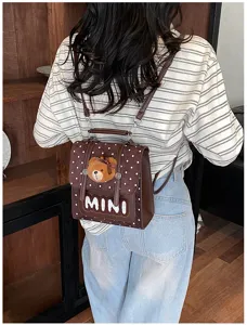 Vue de dos d’une personne portant un mini sac à dos brun à pois avec un pendentif ours en peluche
