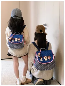 Deux modèles portent des sacs bleus brodés de personnages, avec bord à carreaux et breloques ours