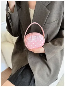 Une main tient un petit sac rond rose à pois blancs, avec dentelle, anse et fermeture zippée