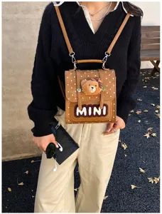 Détail d’un sac brun à pois blancs, avec un ourson en peluche et un écusson MINI, porté devant