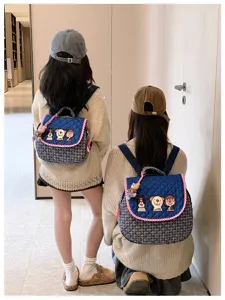 Sacs bleus matelassés avec broderies de personnages, bord rouge et breloque ours, vus de dos