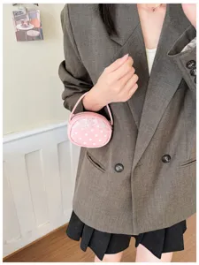 Petit sac ovale rose à pois blancs et bordure en dentelle, tenu par un modèle par sa fine anse