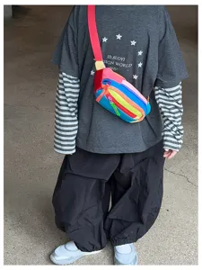 Un enfant porte un sac bandoulière multicolore, à sangle rouge et compartiments zippés