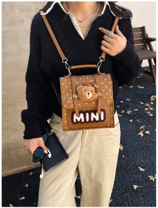 Vue portée en extérieur d’un sac brun à pois blancs, avec ourson décoratif et lettres MINI en relief