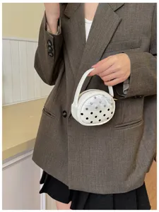 Une personne tient un sac rond blanc à façade en résille à pois, avec poignée et fermeture zippée