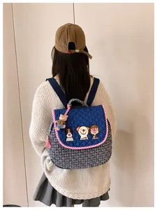 Vue de dos d’un modèle portant un sac matelassé avec écussons illustrés, bord rouge et breloque ours