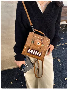 Vue portée d’un sac brun à pois blancs, avec un pendentif ourson en peluche et l’inscription MINI