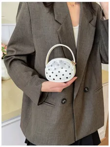 Vue rapprochée d’un sac rond blanc à pois noirs, avec poignée blanche et fermoir doré