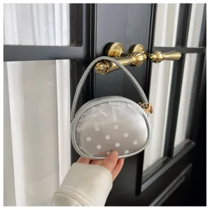 Sac ovale argenté à pois blancs avec empiècement en tulle, tenu par sa poignée en main