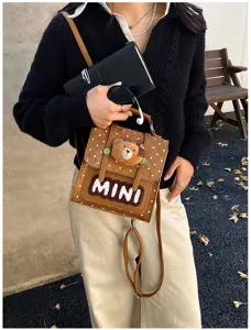 Vue détaillée d’un petit sac brun à pois, avec un pendentif ourson et un écusson MINI bien visible