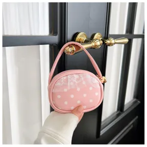 Gros plan sur un petit sac rond rose à pois blancs, bordure en dentelle et breloque cœur dorée