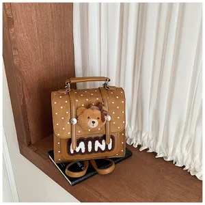Détail d’un sac brun effet daim, à pois blancs, avec pendentif ourson et écusson « MINI »