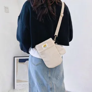 Modèle portant un sac bandoulière ivoire en velours côtelé, rabat en peluche et sangle beige.