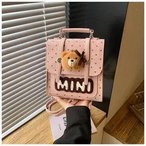 Détail d’un sac rose à pois, avec breloque ourson en peluche, nœud et inscription MINI en relief