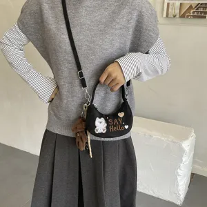Sac noir en croissant avec broderie d’ours et pendentif en peluche, porté par un modèle