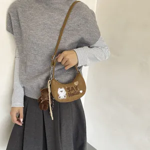 Sac demi-lune brun effet daim avec broderie d’ours, breloque et cordon tressé, porté par un modèle