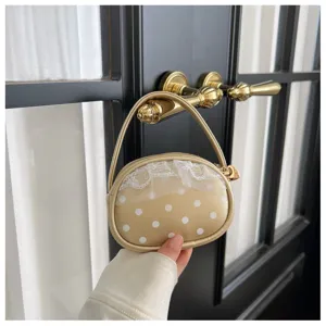 Vue en main d’un petit sac doré arrondi à pois blancs, bordure en dentelle et anse fine