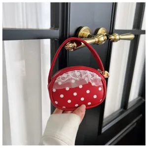 Vue tenue à la main : surface rouge à pois blancs, bordure en dentelle et breloque en cœur