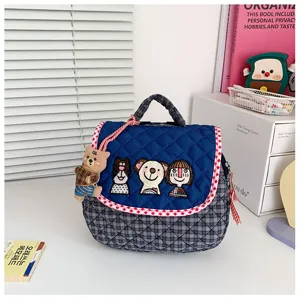 Détail d’un sac bleu matelassé, carreaux, bord rouge et blanc, broderie cartoon et pendentif ourson