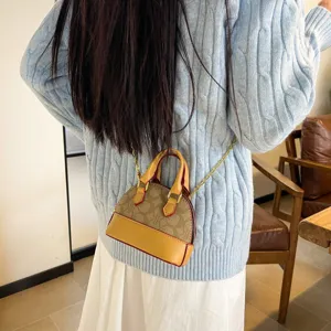 Petit sac bandoulière brun à motifs, bordure jaune et chaîne dorée, porté avec un pull en maille