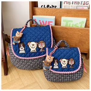 Deux sacs bleu marine matelassés, brodés de personnages, avec bord à pois rouges et breloques ours