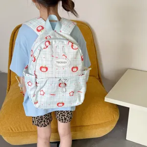 Sac à dos enfant à carreaux bleu clair, motifs de pommes rouges et chats, porté par un enfant