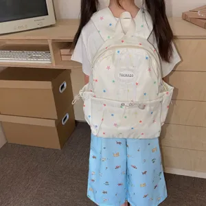Sac à dos enfant crème à étoiles colorées, avec poche zippée sur le devant, porté de face