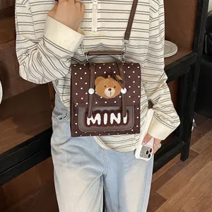 Petit sac bandoulière marron à pois, avec breloque ourson et inscription MINI blanche, porté par un modèle