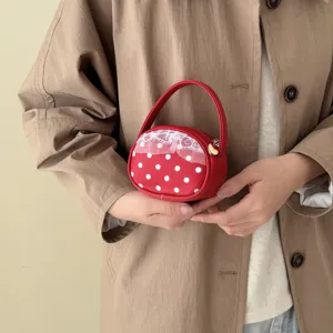 Petit sac rond rouge à pois blancs, dentelle et zip à cœur, présenté dans la main d’un modèle