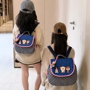 Sac à dos bleu matelassé à carreaux, rabat brodé de personnages et breloque ourson, porté par deux modèles
