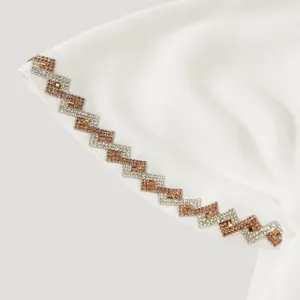 Gros plan sur un bord de tissu blanc avec des strass en losanges, dorés rose et argentés