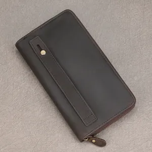 Close-up of a dark brown leather wallet with a vertical strap, metal stud and zip-around edge