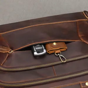 Dettaglio della tasca in pelle marrone vissuta, cuciture beige, zip in ottone e gancio metallico