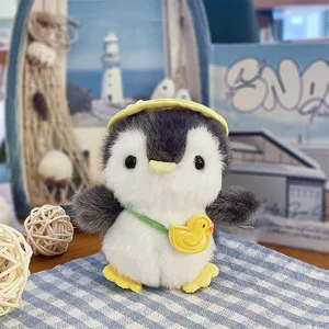 Primo piano di un pinguino di peluche grigio e bianco, con cappello giallo e ciondolo a papera.