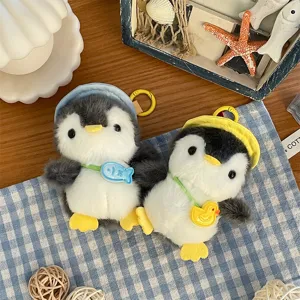 Due pinguini di peluche con cappelli blu e gialli e ciondoli a forma di pesce e anatra