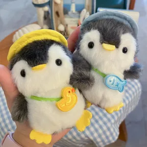 Primo piano di due pinguini di peluche con cappelli colorati e ciondoli a forma di anatra e pesce