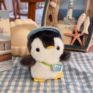 Dettaglio del pinguino di peluche con berretto blu e ciondolo pesce su tessuto a quadretti blu