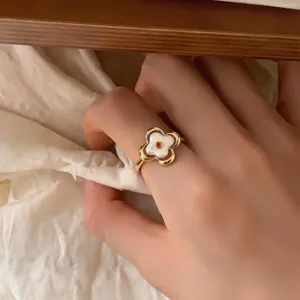 Primer plano de una mano con anillo floral dorado, pétalos nacarados y centro de color naranja