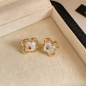 Primer plano de pendientes dorados de flor, con perlas blancas irregulares y pequeñas piedras naranjas