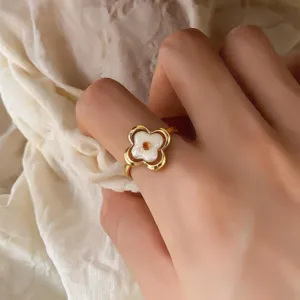 Primer plano de una mano con anillo abierto dorado, flor blanca de cuatro pétalos y piedra naranja