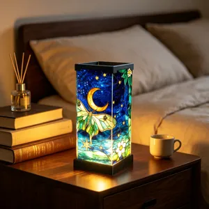 Glowing stained-glass lamp with moon and moth motif on a bedside table beside books
