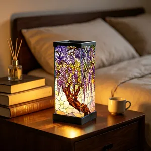 Stained-glass shade with purple flowering vines and a brown tree trunk, glowing on a bedside table