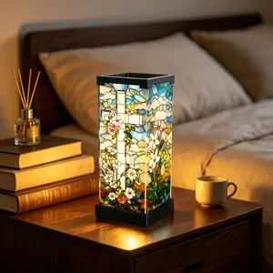 Warm licht schijnt door een glas-in-loodpatroon met kruis en bloemen op een nachtkastje naast het bed