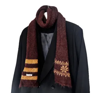 Longue écharpe en maille rouge bordeaux, à rayures jaunes et flocons, portée sur un manteau sombre