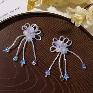 Paired white beaded flowers with blue star and crystal teardrop charms arranged on a dark tray