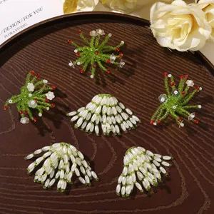 Overhead view of five beaded ornaments: green starbursts and white pearl fans with red accents
