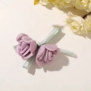 Zwei mauvefarbene Satinrosen mit hellgrünen Schleifen, flach auf einer hellen Tischfläche arrangiert