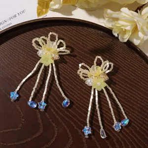 Flat lay of cream bead strands, pale yellow flowers, pearls and blue glass drops on dark wood