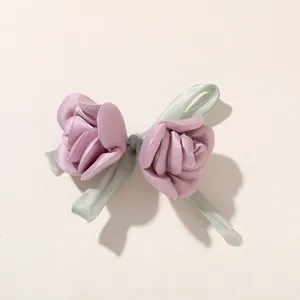 Zwei lavendelfarbene Satinrosen mit blass salbeigrünen Bandschleifen auf elfenbeinfarbenem Grund